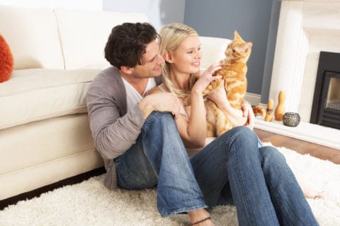 A man and woman sitting on the floor with a cat.