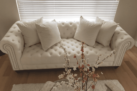 A white couch with pillows and a vase of flowers.